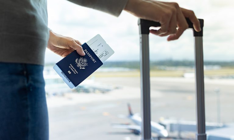 Figura di uomo in aeroporto che tiene un trolley e un passaporto