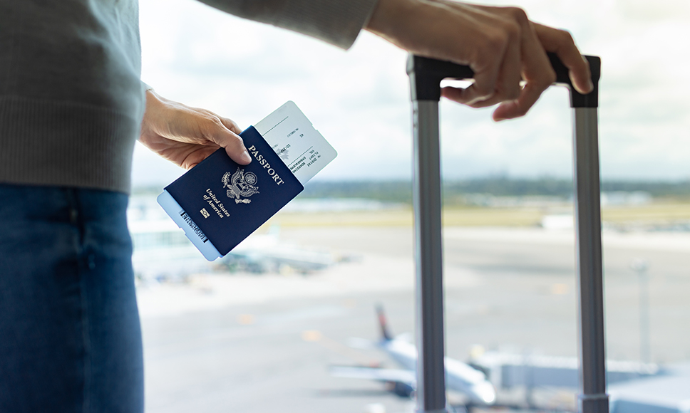 Figura di uomo in aeroporto che tiene un trolley e un passaporto