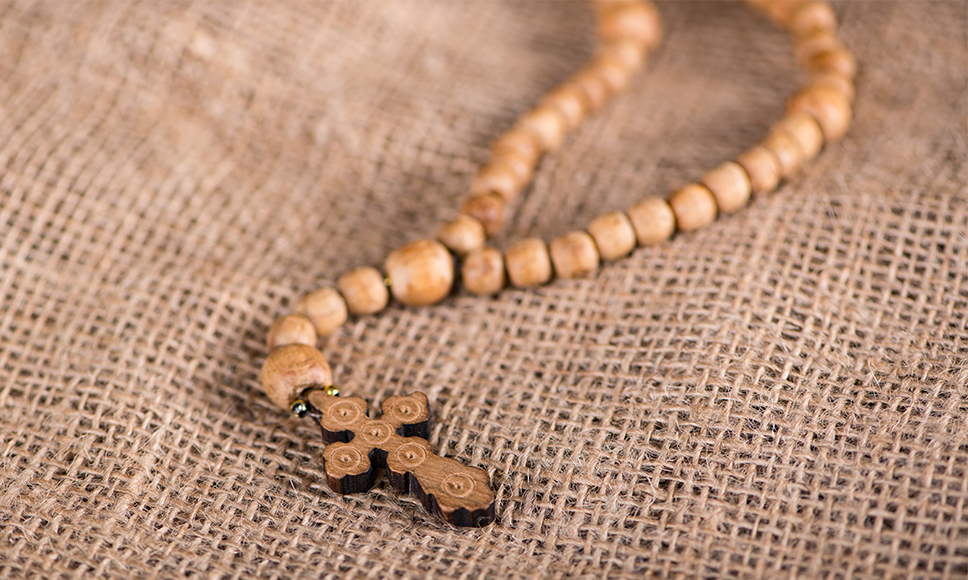 Un rosario di legno con una croce, appoggiato su un tessuto di tela.